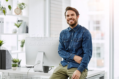 Buy stock photo Cropped portrait of a handsome young businessman smiling while sitting on his desk in a modern office