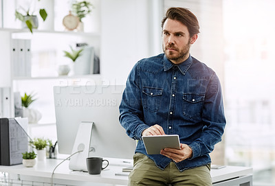 Buy stock photo Cropped shot of a handsome young businessman looking thoughtful while using a digital tablet in his office