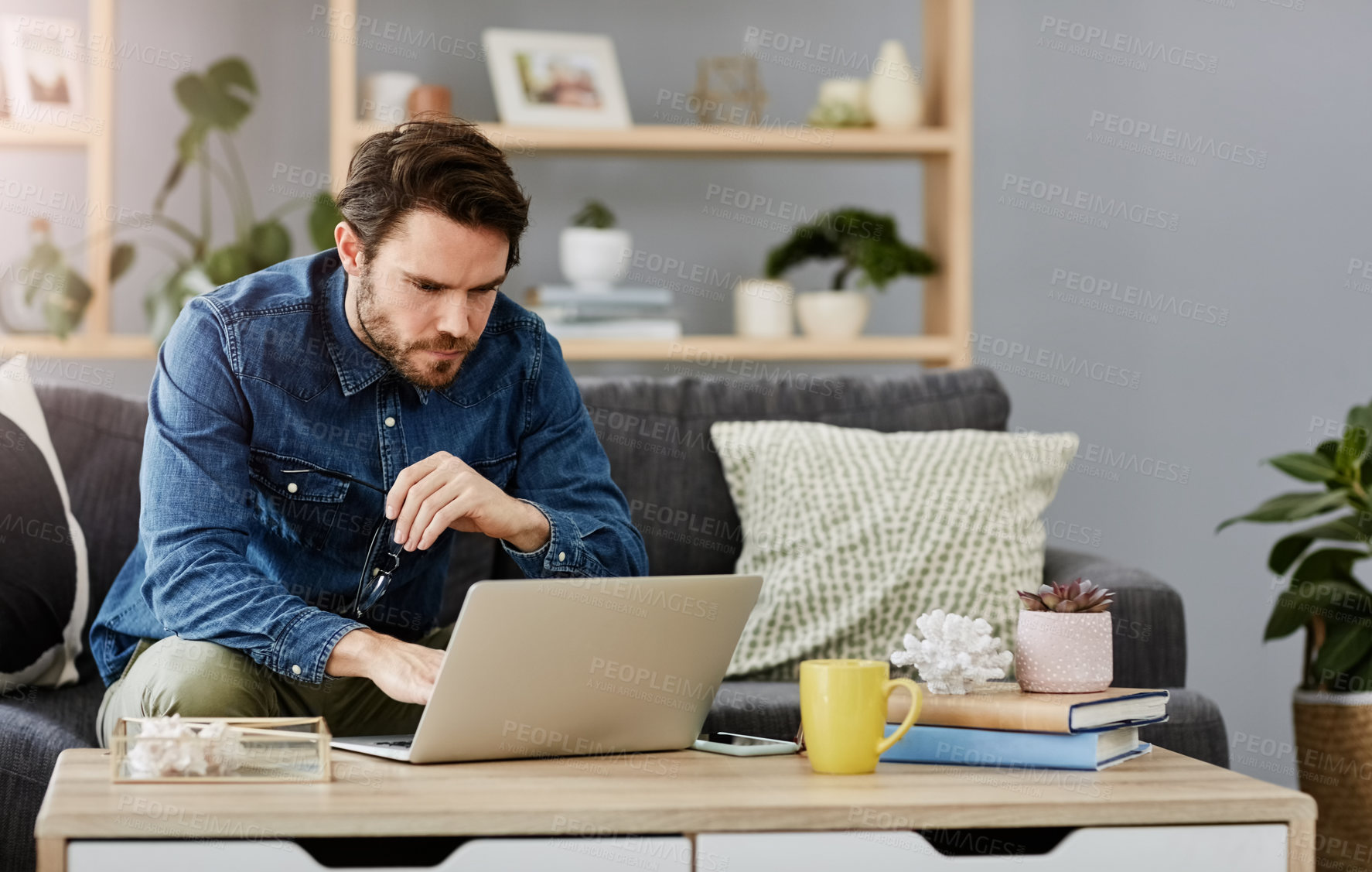 Buy stock photo Cropped shot of a handsome young man using a laptop in his living room at home