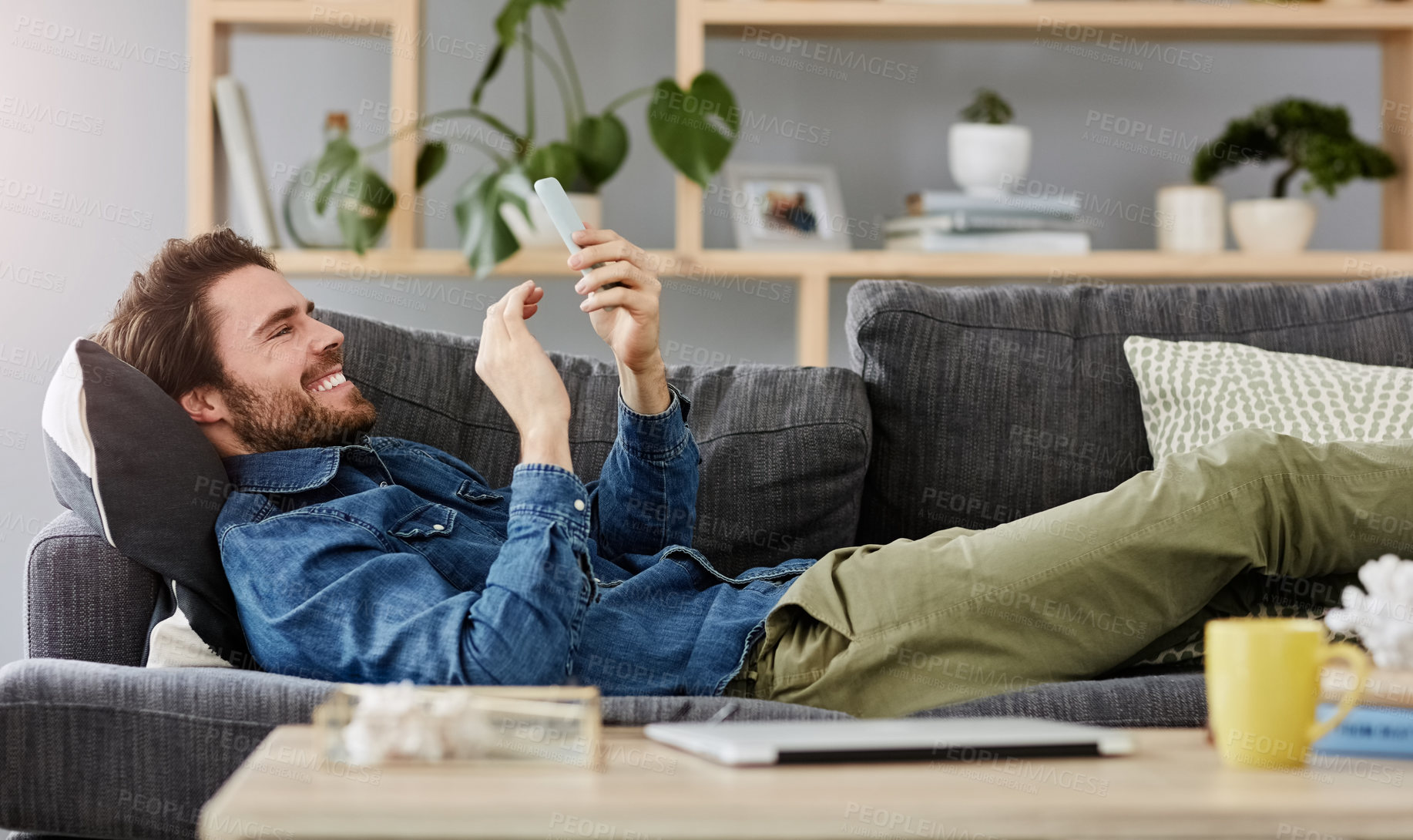 Buy stock photo Social networking, man with smartphone on sofa and lying in living room at his home. Connectivity or technology, smile and happy male person with cellphone comfortable on couch playing online game
