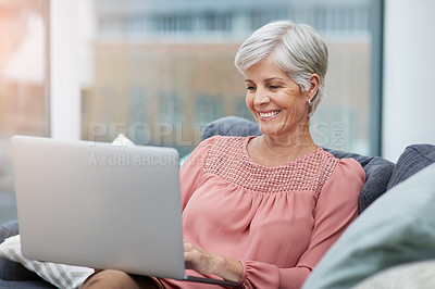 Buy stock photo Shot of a cheerful mature woman using her laptop while relaxing on her sofa ta home