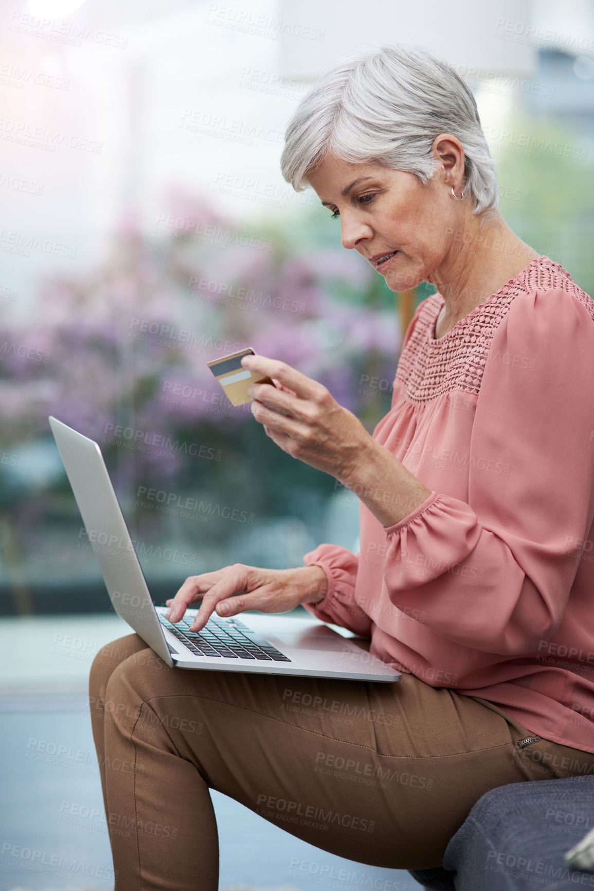 Buy stock photo Shot of a mature woman using her laptop while holding her credit card at home