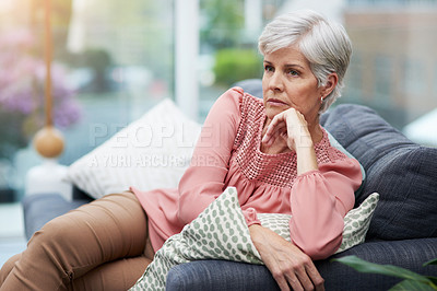 Buy stock photo Shot of a mature woman looking thoughtful while relaxing on her couch at home