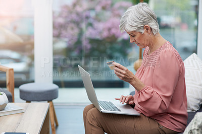 Buy stock photo Shot of a mature woman sitting on a couch and using her laptop to do some online shopping at home