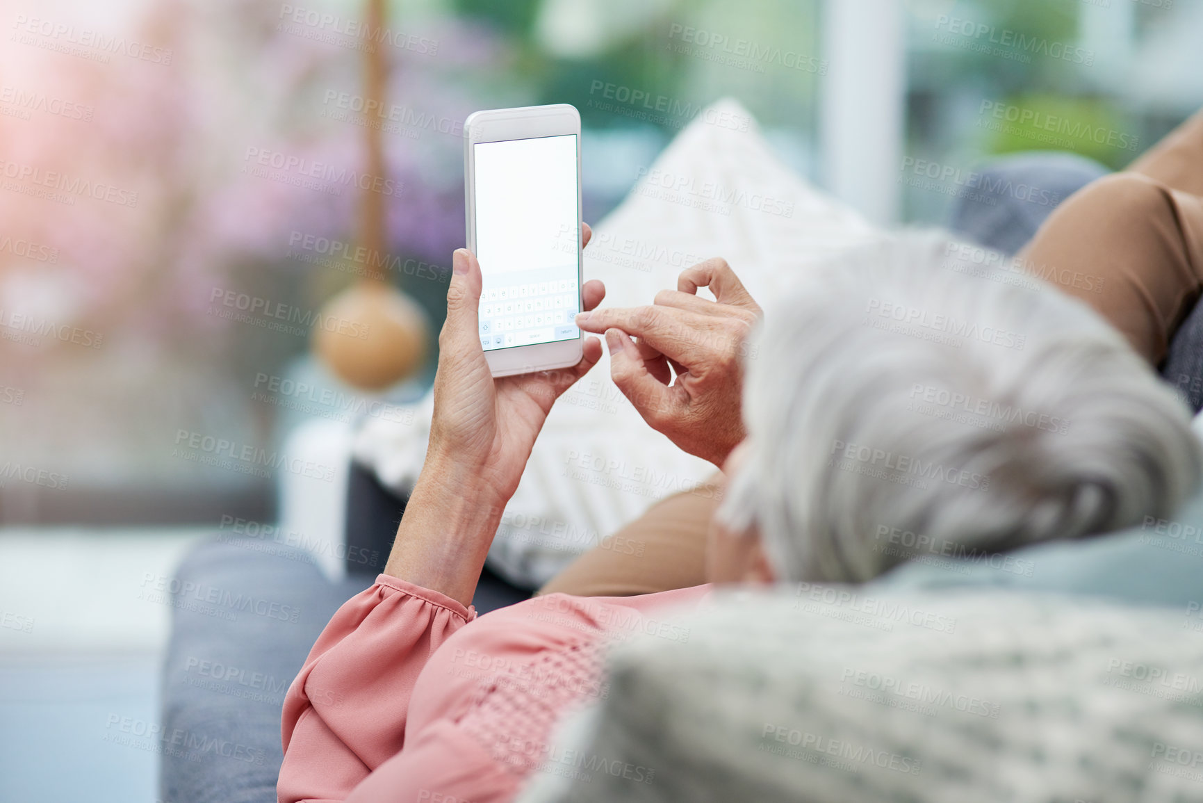 Buy stock photo Rearview shot of a mature woman using her cellphone while relaxing on a sofa at home