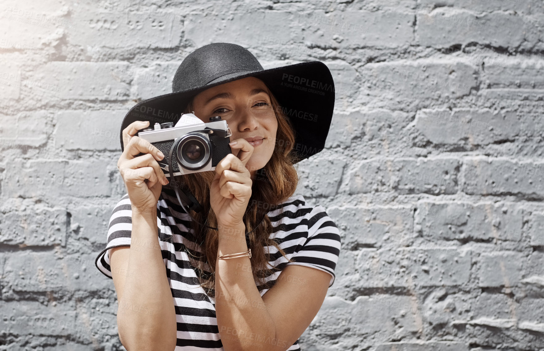 Buy stock photo Shot of a young woman taking a picture with her camera against a brick wall outdoors