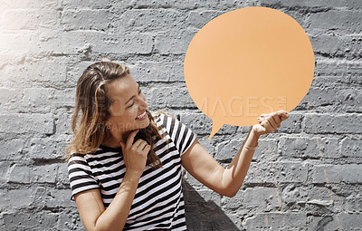 Buy stock photo Shot of a cheerful young woman holding a speech bubble against a brick wall outside