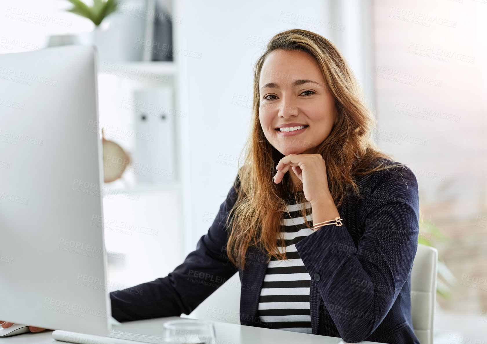 Buy stock photo Portrait of a cheerful businesswoman posing with her hand on her chin while working on a computer in her office