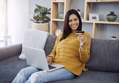 Buy stock photo Shot of an attractive young woman doing some online shopping on her laptop while relaxing on a sofa at home