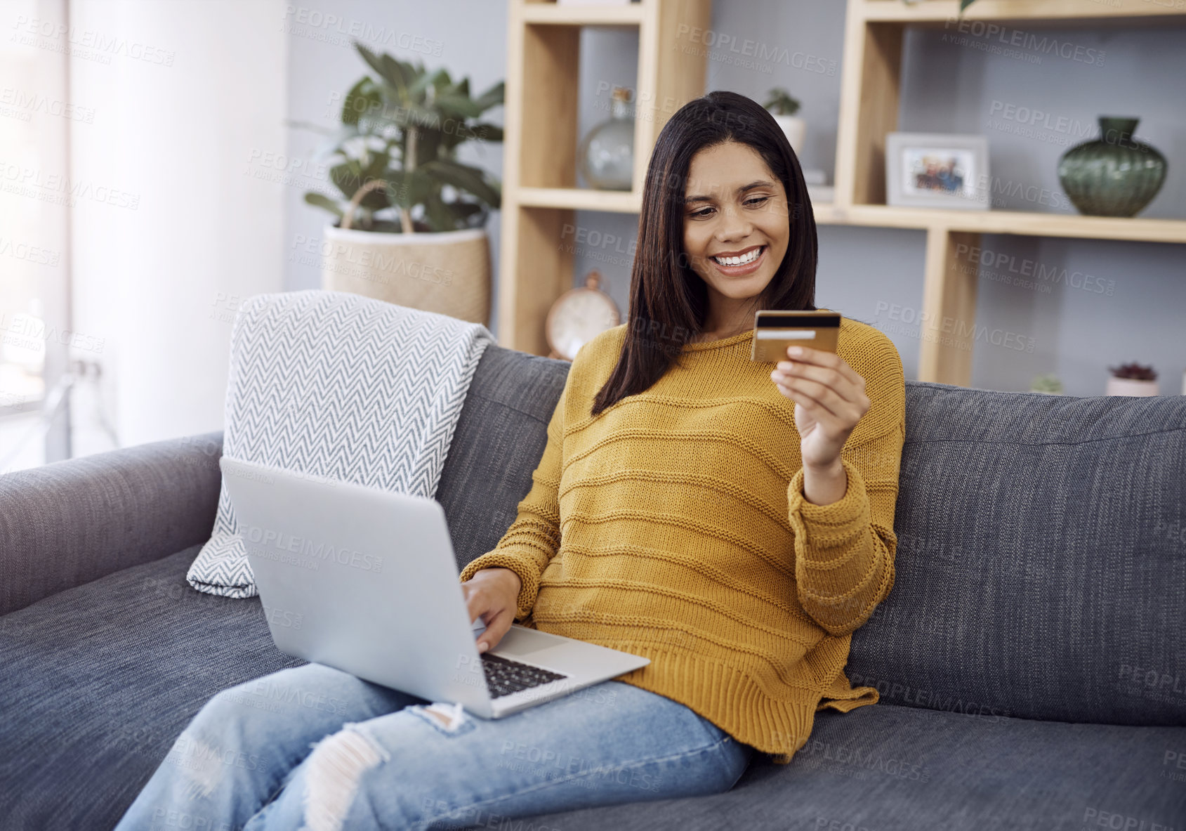 Buy stock photo Shot of an attractive young woman doing some online shopping on her laptop while relaxing on a sofa at home