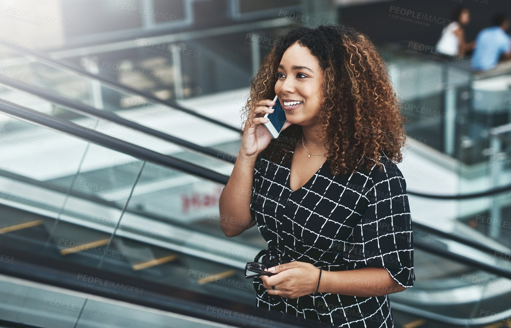 Buy stock photo Cropped shot of an attractive young businesswoman taking a phonecall while moving up an escalator in a modern workplace