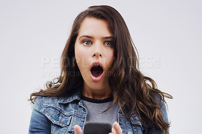 Buy stock photo Shot of a young woman looking surprised while reading something on her cellphone
