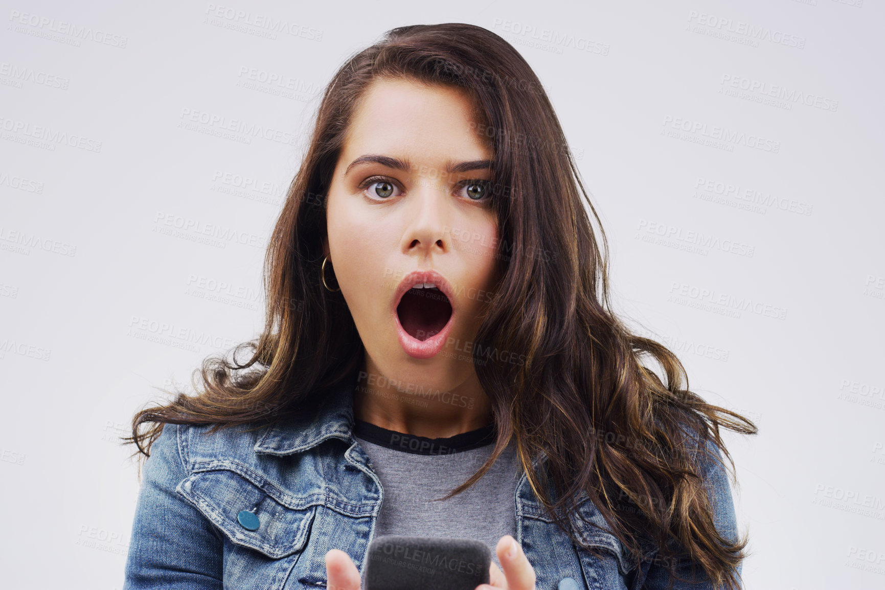 Buy stock photo Shot of a young woman looking surprised while reading something on her cellphone