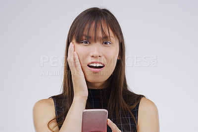 Buy stock photo Studio shot of a young woman looking surprised while reading something on her cellphone