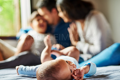 Buy stock photo Shot of an adorable baby boy laying on the floor with his family in the background