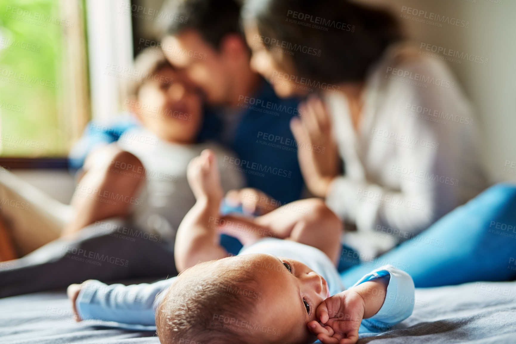 Buy stock photo Shot of an adorable baby boy laying on the floor with his family in the background