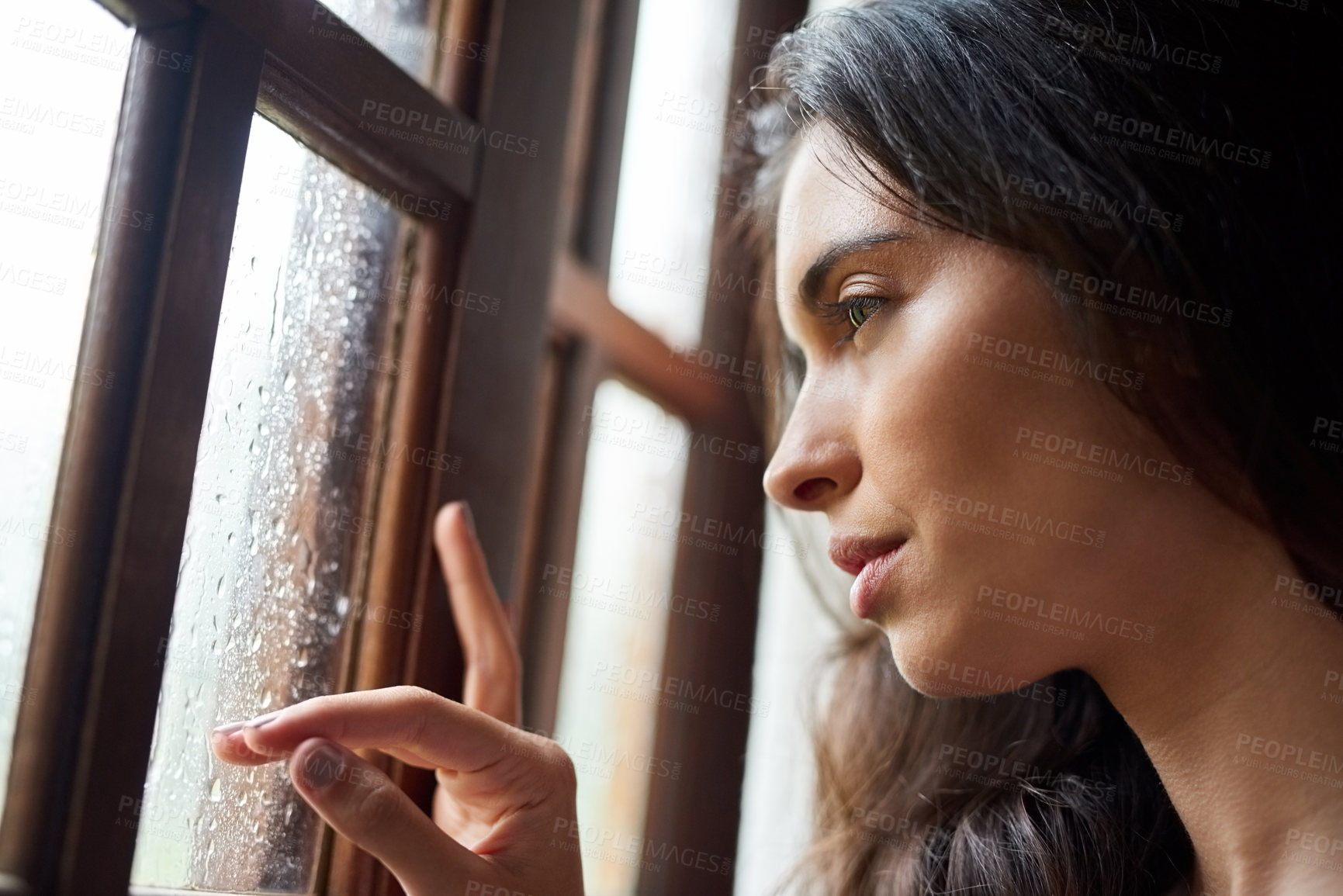 Buy stock photo Shot of an attractive young woman looking out the window at home
