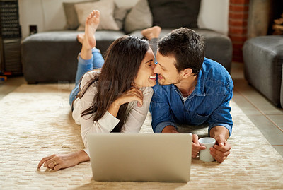 Buy stock photo Shot of an affectionate young couple lying down on the carpet and using their laptop at home