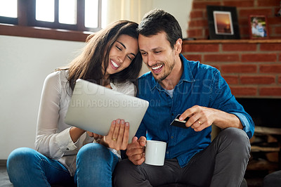 Buy stock photo Shot of an affectionate young couple using a digital tablet together while relaxing at home