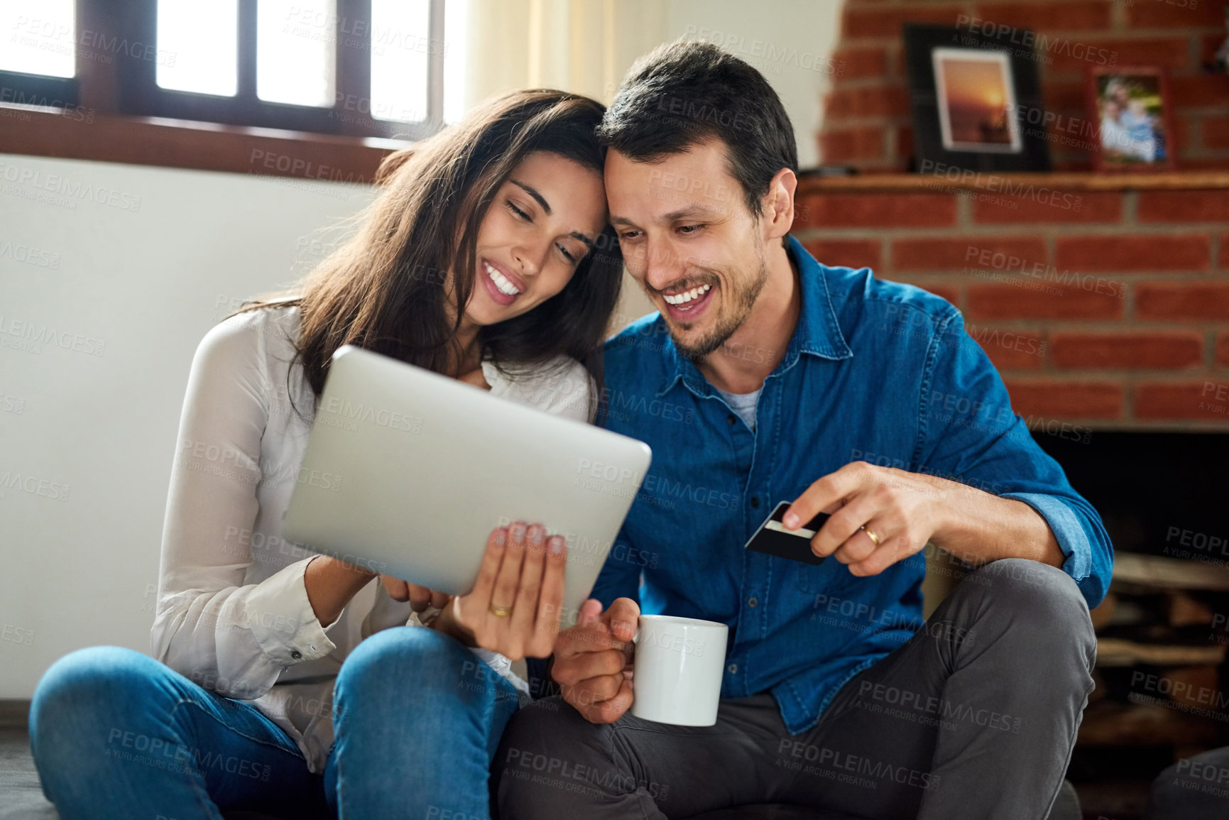 Buy stock photo Shot of an affectionate young couple using a digital tablet together while relaxing at home