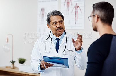 Buy stock photo Shot of a confident mature male doctor consulting a patient  inside a hospital during the day