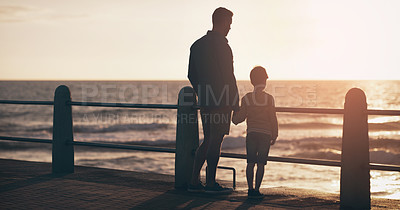 Buy stock photo Silhouette, sunset and a father holding hands with his son on the promenade at the beach while walking together. View, family or kids and a man bonding with his young male child outdoor in nature