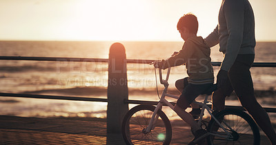 Buy stock photo Father, boy and bike for teaching at beach, promenade and sunset on vacation with care, love and bonding. Man, child and bicycle with support, learning and outdoor by sea, waves and holiday in summer