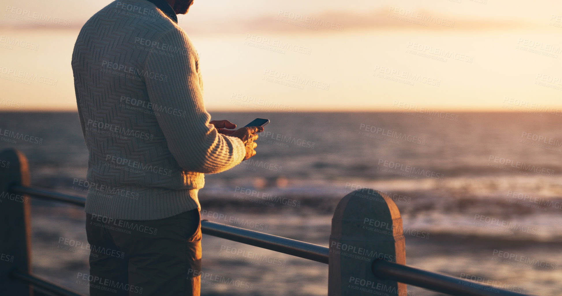 Buy stock photo Man, phone and texting on promenade by ocean with sunset sky on vacation with contact on web. Person, smartphone and outdoor by sea, waves and back on holiday by horizon with app for social media