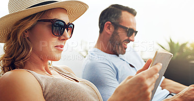 Buy stock photo Shot of a mature couple sitting side by side on deck chairs and doing some reading outdoors while on holiday