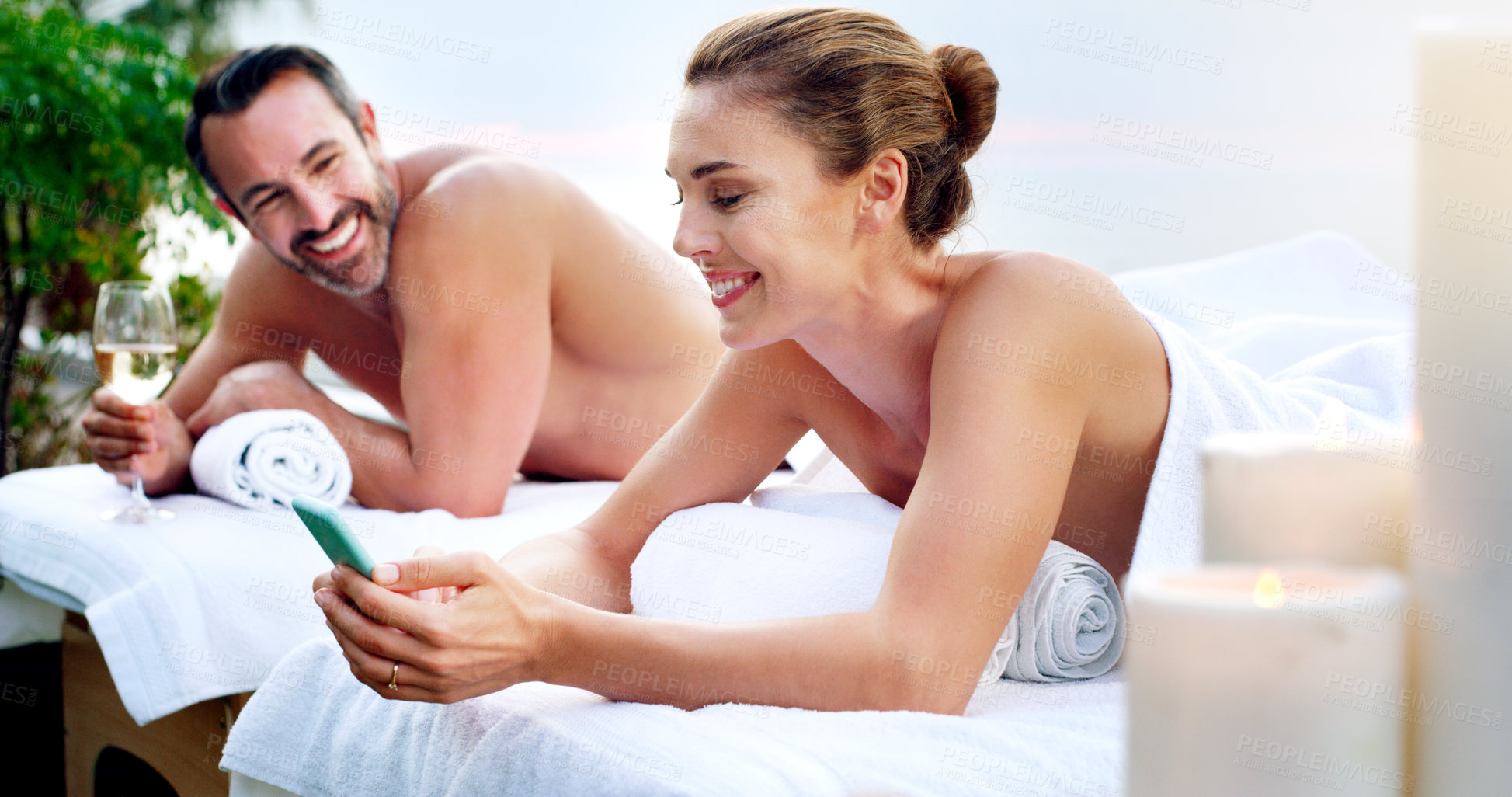 Buy stock photo Couple, spa and massage table for outdoor treatment with cellphone or champagne, skincare or stress relief. Man, woman and zen resort for honeymoon travel for beauty wellness, texting or social media