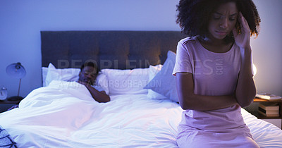 Buy stock photo Shot of a concerned looking young woman sitting on a bed with her husband sleeping in the background