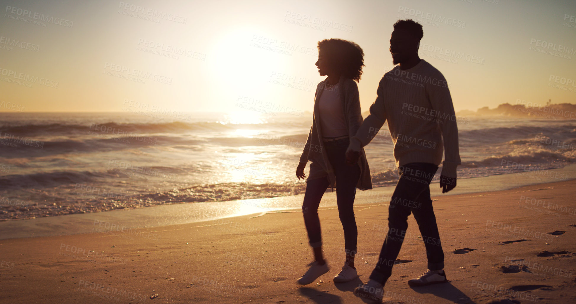 Buy stock photo Full length shot of an affectionate young couple taking a stroll on the beach at sunset