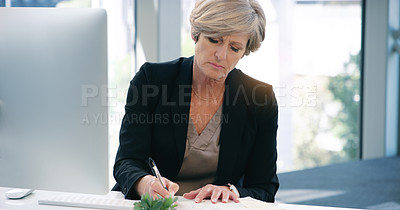 Buy stock photo Shot of a mature businesswoman writing notes while working on a computer in an office