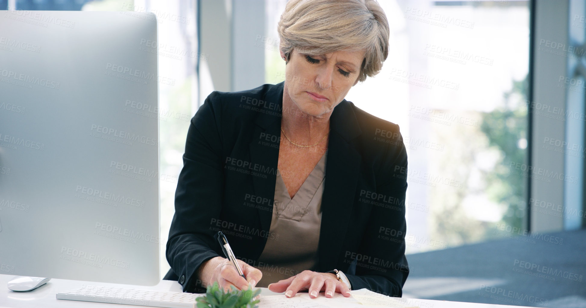 Buy stock photo Shot of a mature businesswoman writing notes while working on a computer in an office