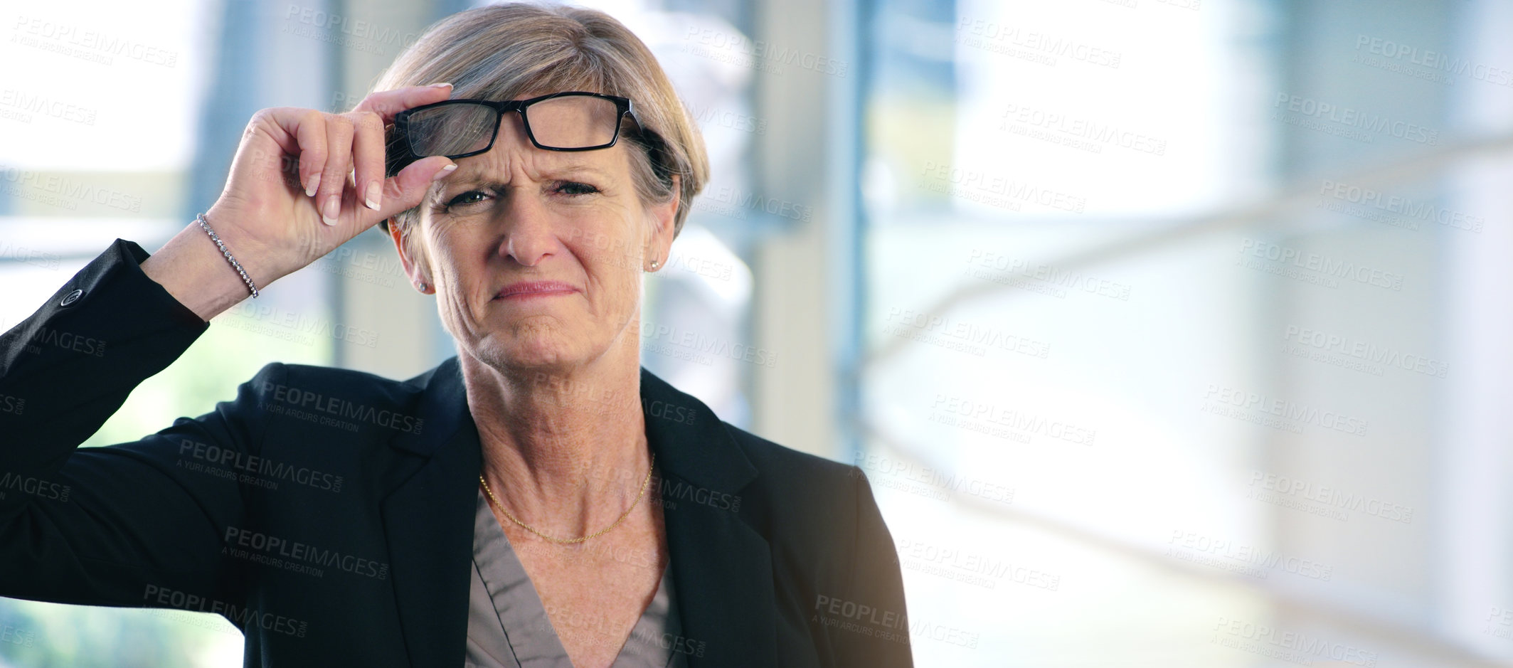 Buy stock photo Portrait of a mature businesswoman frowning while holding a pair of spectacles in an office