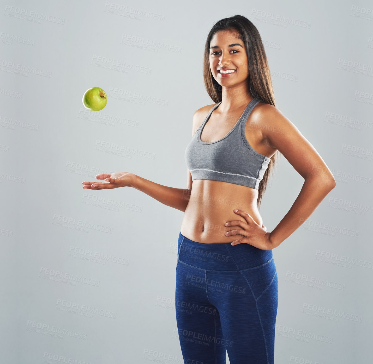 Buy stock photo Cropped studio portrait of a happy young woman throwing an apple against a gray background