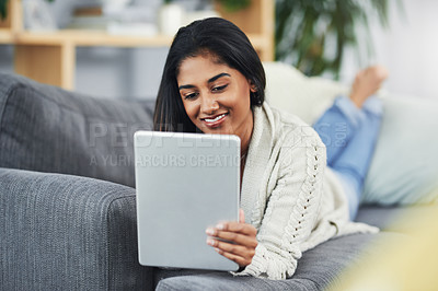 Buy stock photo Shot of an attractive young woman using her digital tablet while relaxing on he couch at home