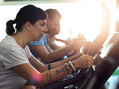 Buy stock photo Shot of a group of young people working out on elliptical machines in the gym