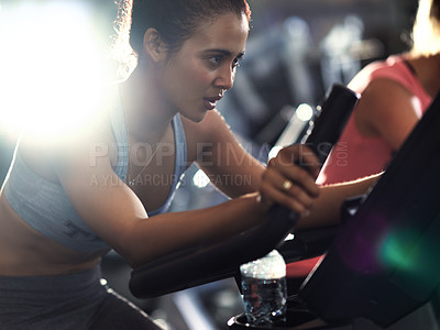 Buy stock photo Shot of a determined looking young woman working out on an elliptical machine in the gym