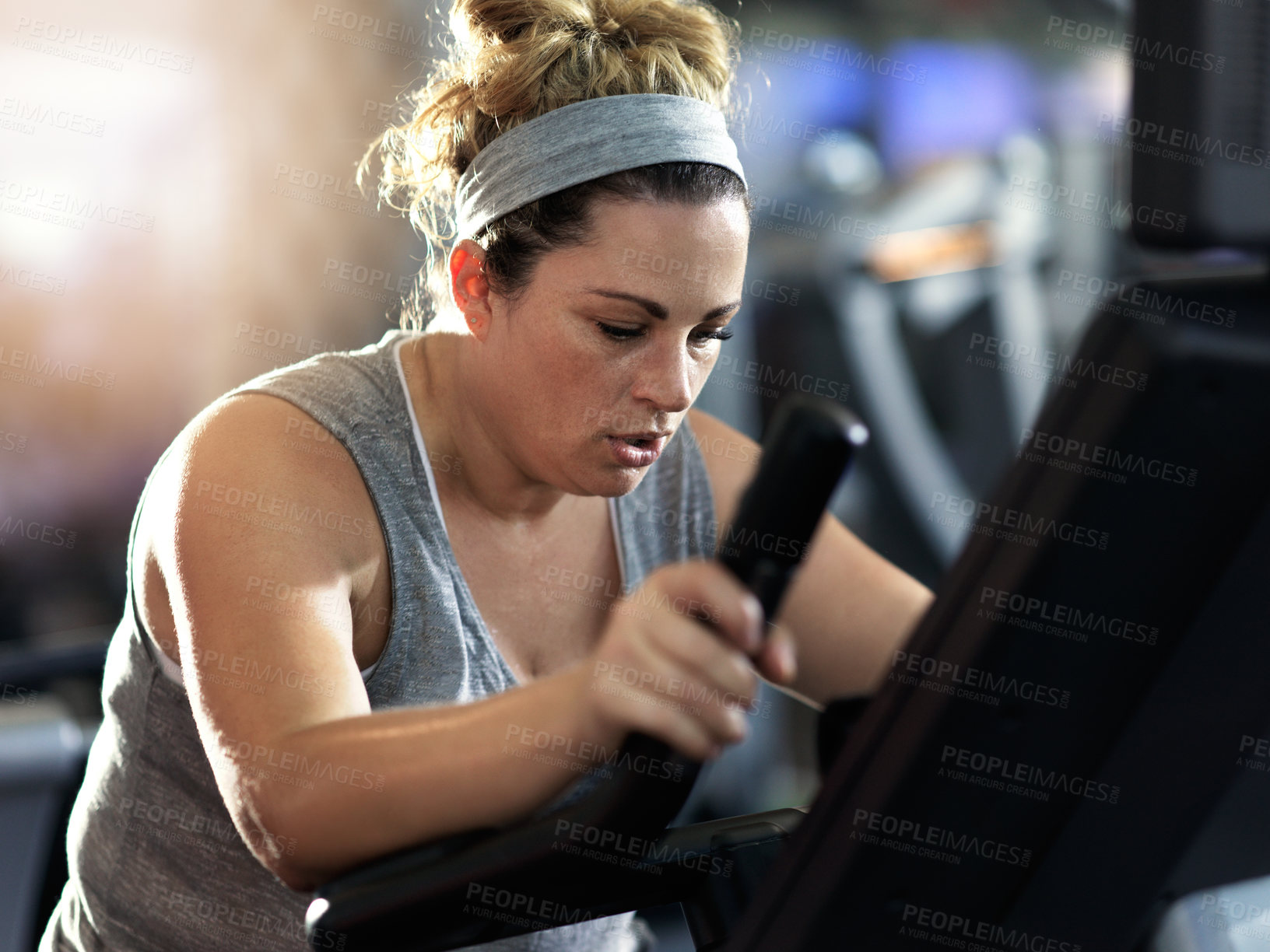 Buy stock photo Shot of a determined looking woman working out on an elliptical machine in the gym