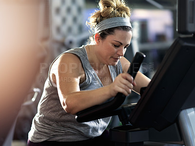Buy stock photo Shot of a determined looking woman working out on an elliptical machine in the gym