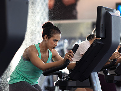 Buy stock photo Shot of a determined looking young woman working out on an elliptical machine in the gym