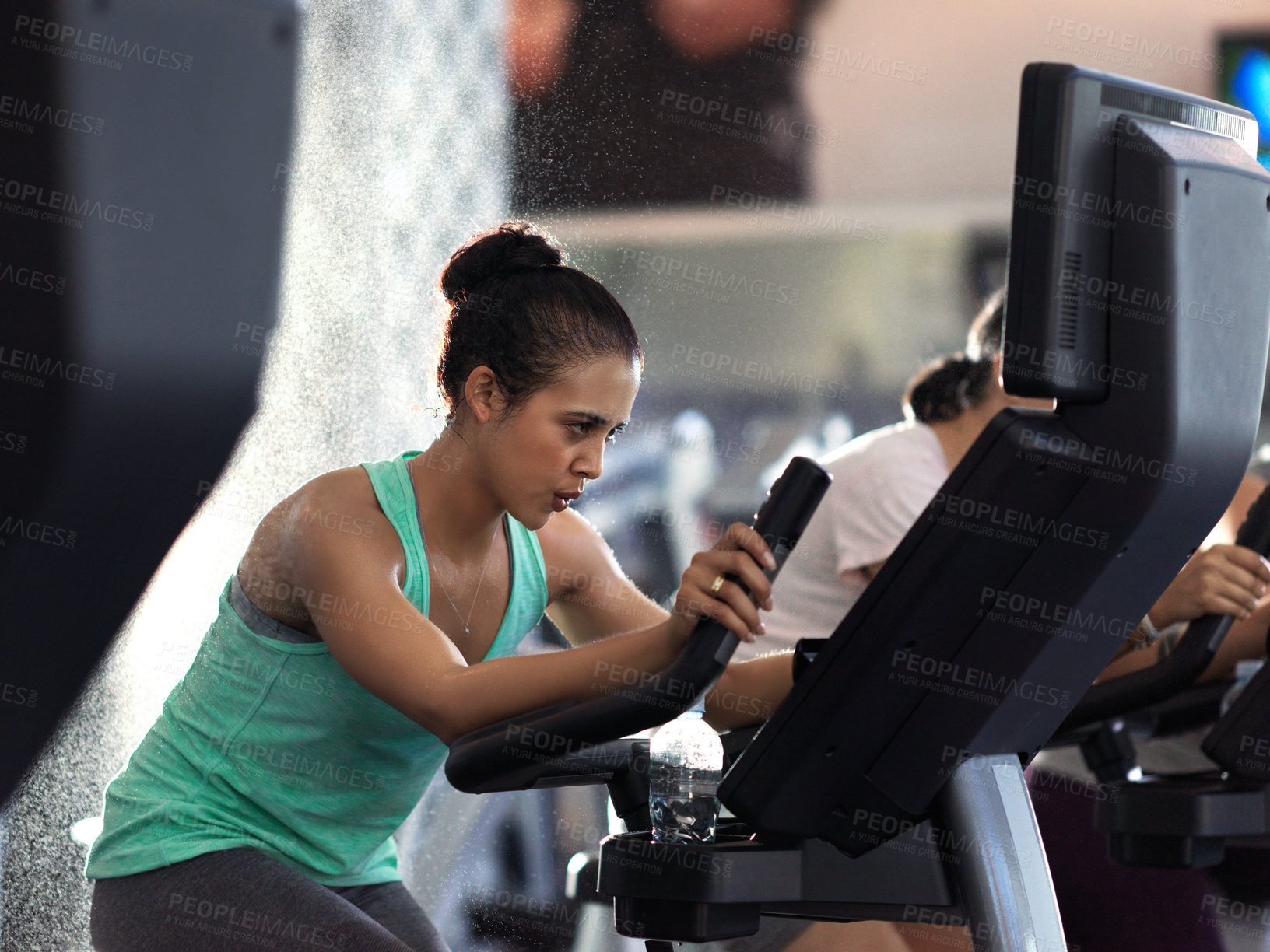 Buy stock photo Shot of a determined looking young woman working out on an elliptical machine in the gym