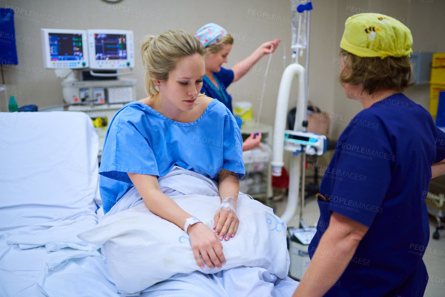 Buy stock photo Shot of a young pregnant woman sitting on her hospital bed and looking thoughtful with nurses in the background