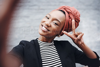 Buy stock photo Cropped portrait of an attractive young businesswoman taking selfies while gesturing the peace sign against a grey brick wall outside