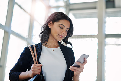 Buy stock photo Cropped shot of an attractive young businesswoman using a smartphone while standing in a modern office