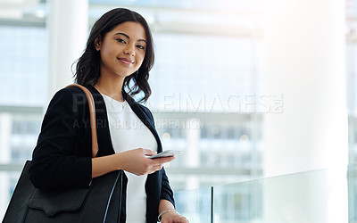 Buy stock photo Cropped portrait of an attractive young businesswoman holding a smartphone while standing in a modern office