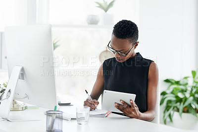 Buy stock photo Shot of a confident young businesswoman writing in a notebook and using a digital tablet in a modern office