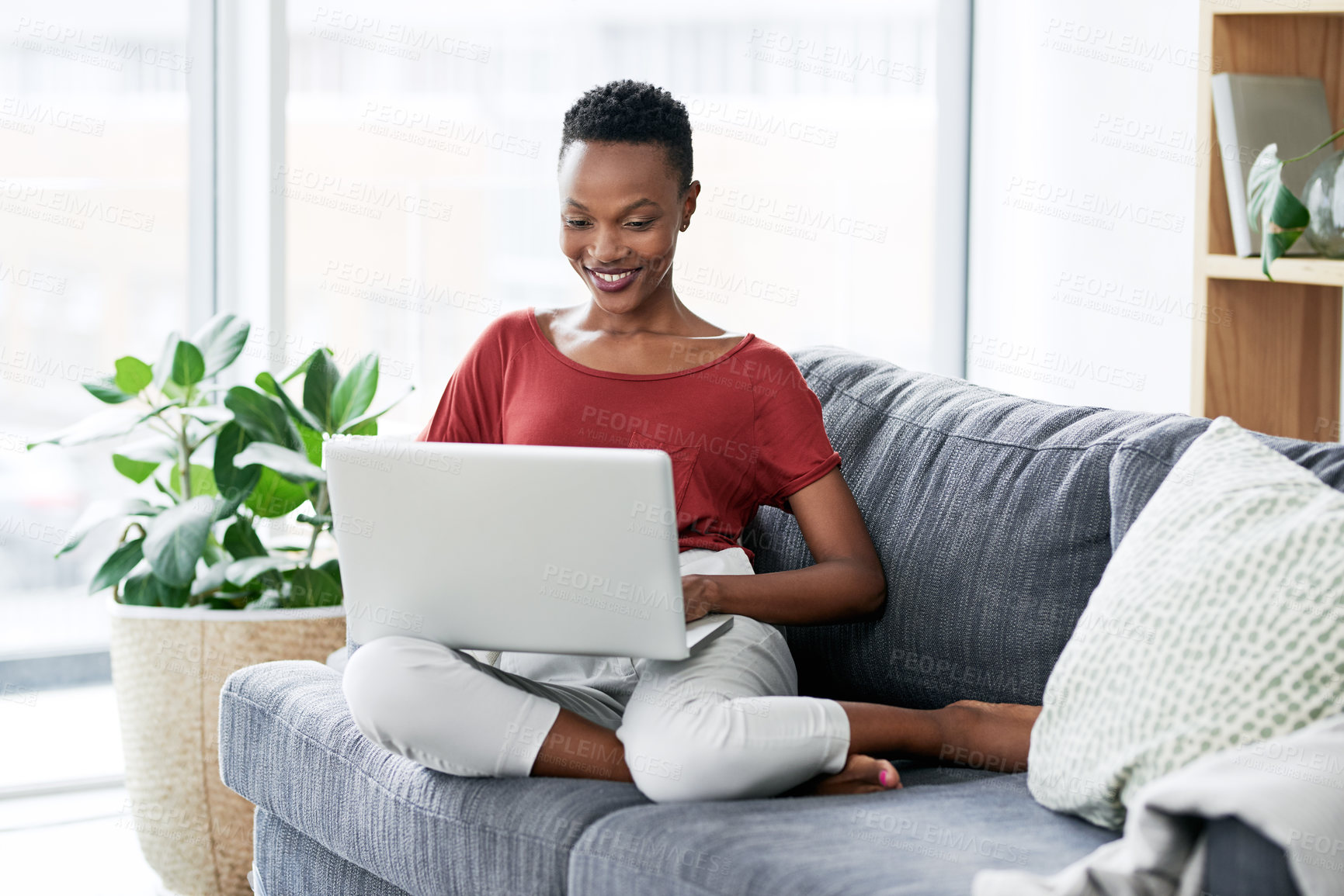 Buy stock photo Shot of a young woman relaxing on the sofa at home and using a laptop