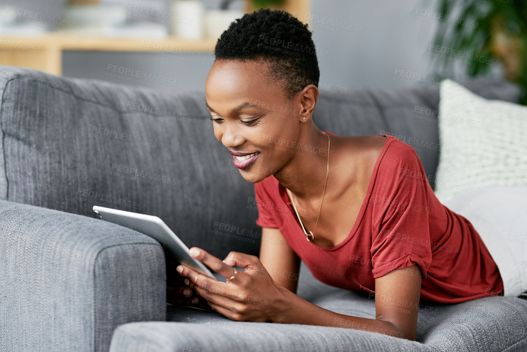 Buy stock photo Shot of a young woman relaxing on the sofa at home and using a digital tablet
